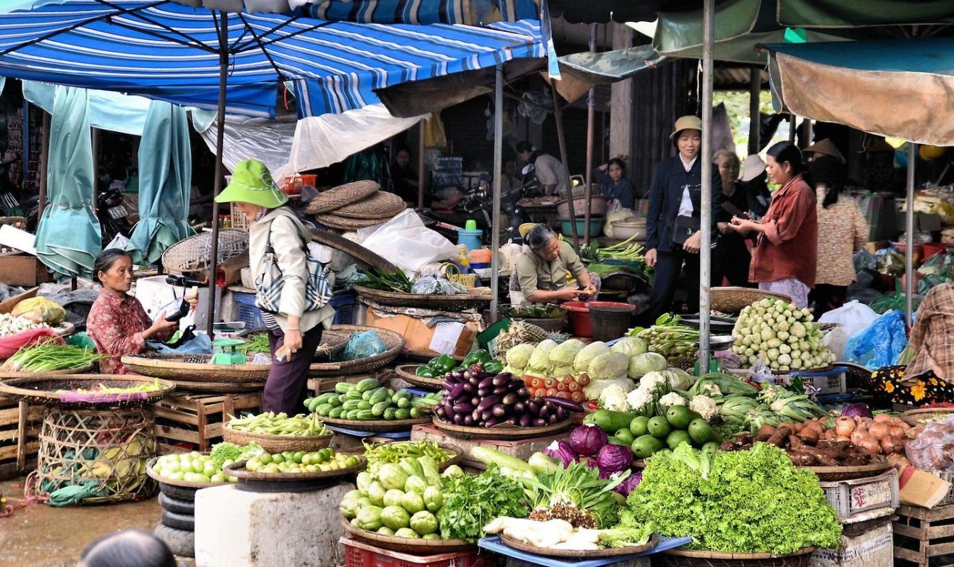 Vibrant market scene in Vietnam with vendors selling fresh produce and customers enjoying pho.