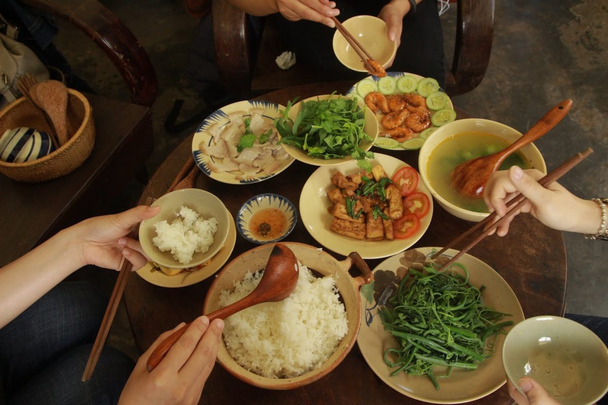 People sharing a meal with various dishes, including pho, on a wooden table in Vietnam.