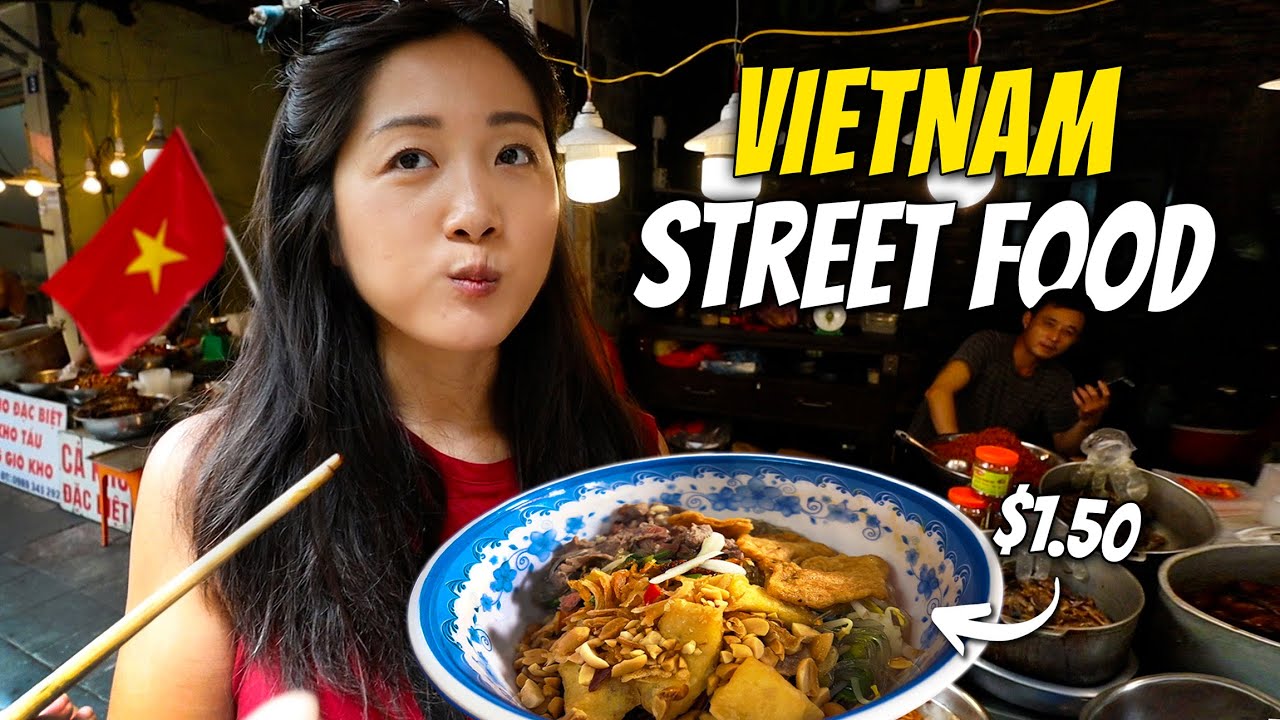 A woman sampling Vietnamese pho street food with a price label, as a vendor looks on in the background.