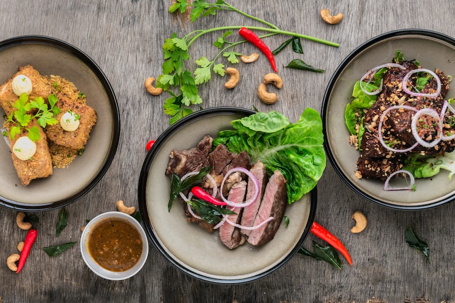 Three bowls of various Asian dishes, including Pho from Vietnam, garnished with herbs and spices on a wooden surface.