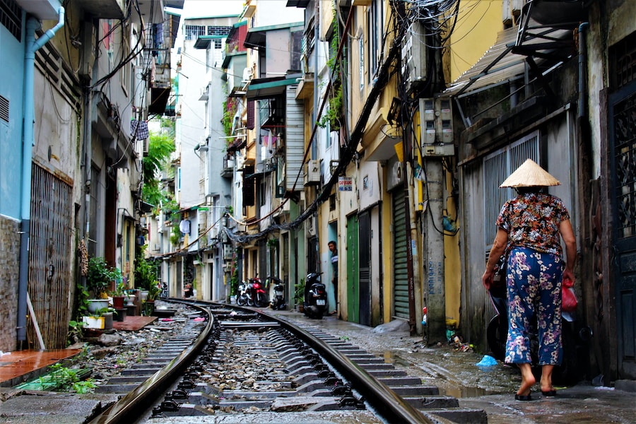 Narrow urban alley in Vietnam with train tracks and a person walking away wearing a conical hat.