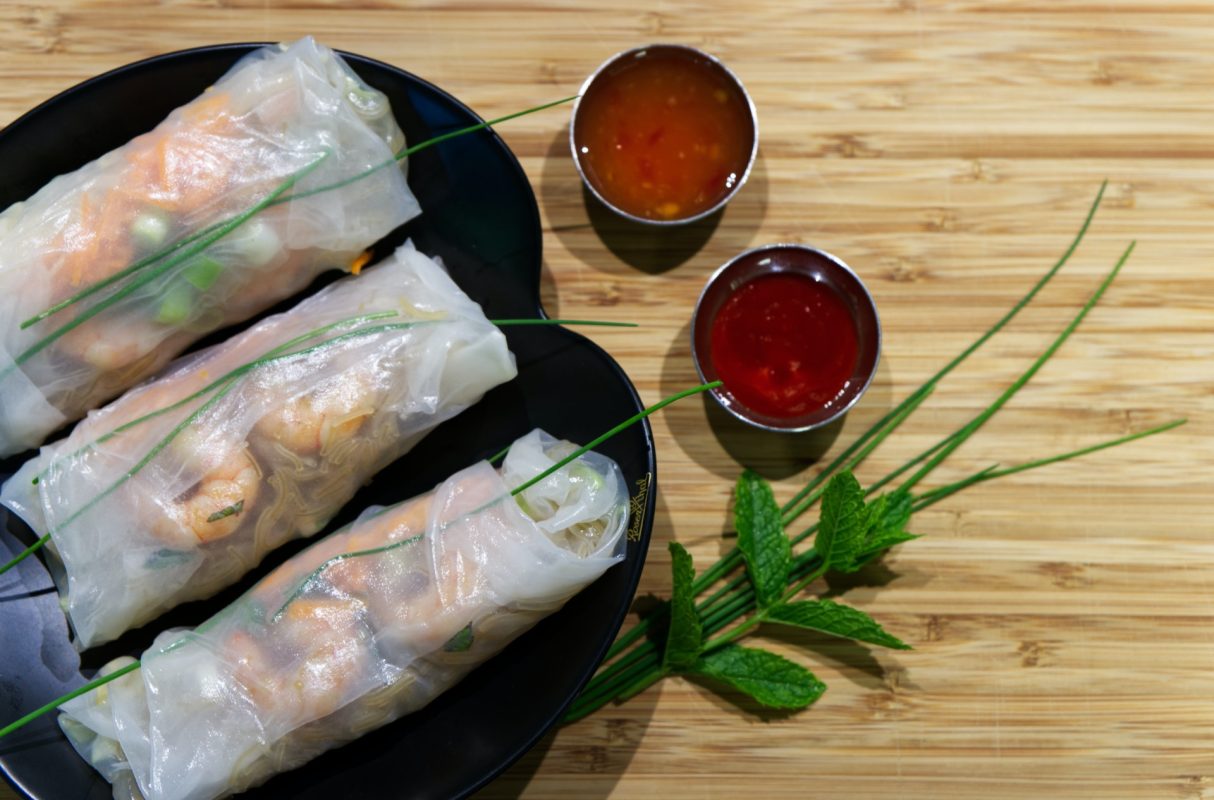 Fresh spring rolls with shrimp and dipping sauces on a wooden table, a delicacy from Vietnam.