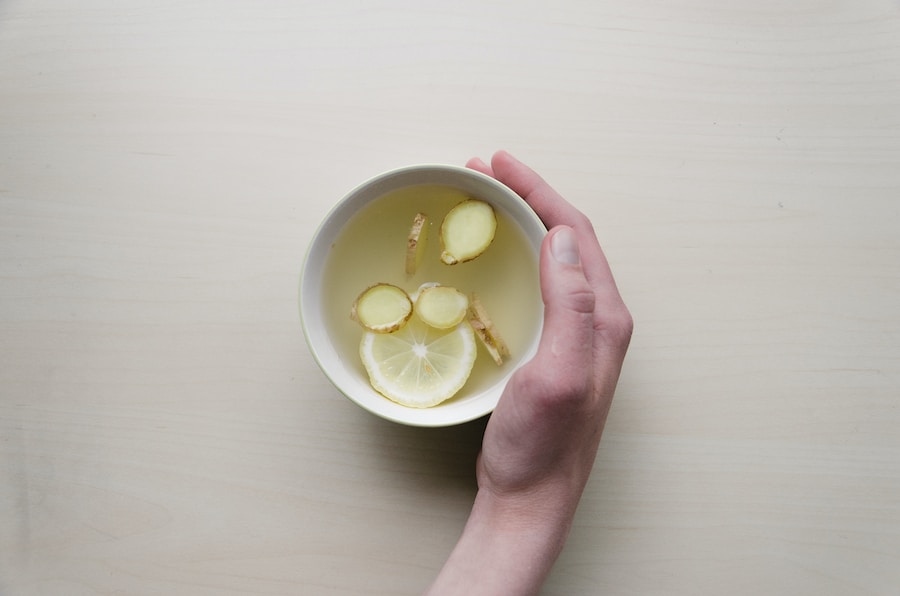 A hand holding a bowl with lemon and ginger slices, pho spices on a wooden surface.