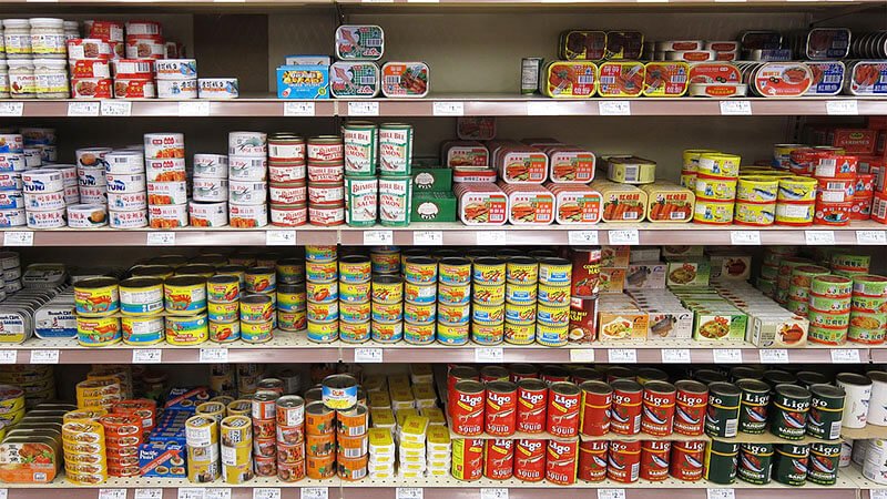 Shelves stocked with a variety of canned food products, including pho from Vietnam, at a grocery store.