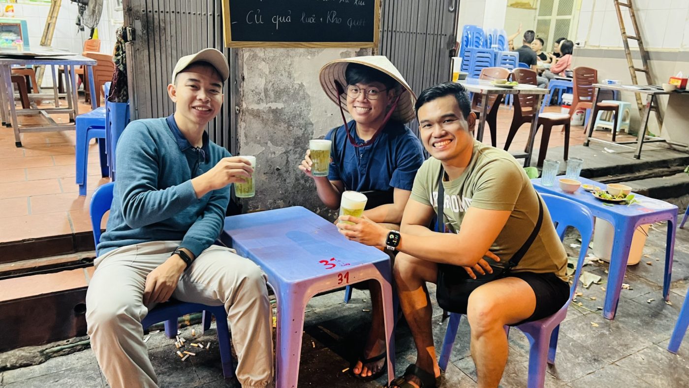 Three friends enjoying drinks at an outdoor table in a casual street dining setting in Vietnam.