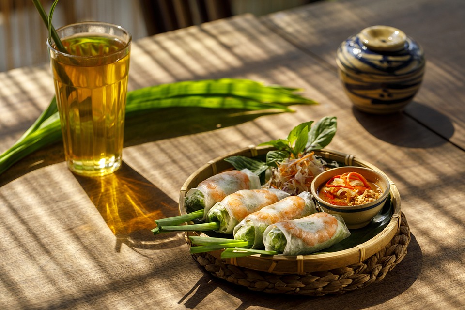 Vietnamese spring rolls served with herbs, dipping sauce, and a glass of tea on a wooden table in Vietnam.