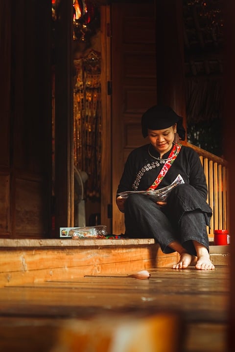 A person sits on a wooden porch step in Vietnam, intently working on a craft project.