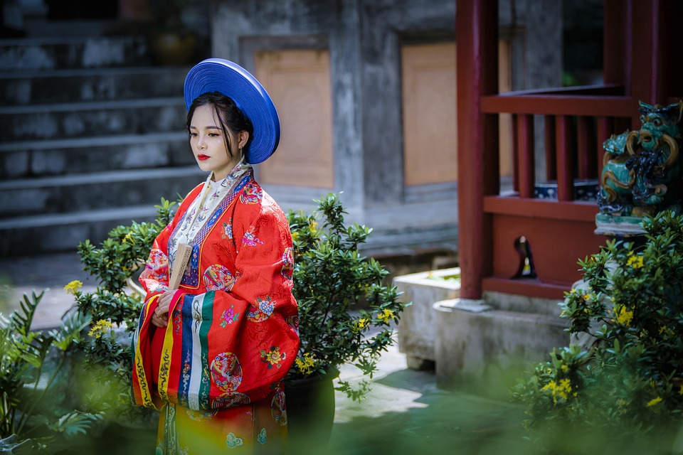 A woman in traditional Vietnamese attire stands contemplatively in a serene garden setting, reminiscent of the tranquil beauty found in Vietnam.