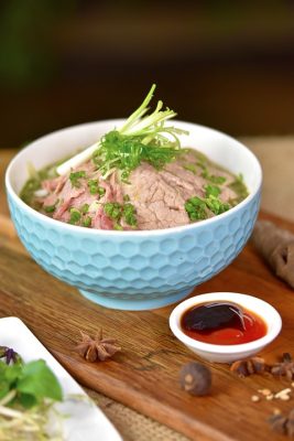 Bowl of Vietnamese pho with sliced beef and herbs, accompanied by a side of hoisin sauce.