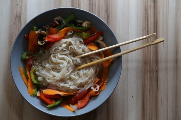 A bowl of Vietnamese pho noodle soup with vegetables and chopsticks on a wooden surface.